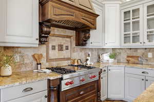 Kitchen featuring light stone counters, glass insert cabinets, and white cabinetry