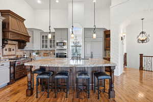 Kitchen with suspended lighting, glass fronted cabinets, dual tone cabinets, stainless steel appliances, and light stone countertops