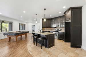 Kitchen featuring stainless steel appliances, light stone countertops, billiards, a kitchen bar, and hanging light fixtures
