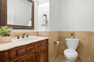 Half bath featuring vanity, wainscoting, and tile walls