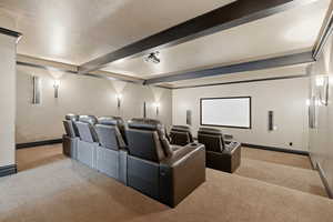 Cinema featuring light carpet, beam ceiling, and a textured ceiling