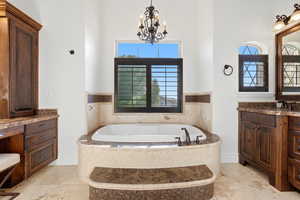 Bathroom featuring vanity, a bath, a chandelier, a high ceiling, and healthy amount of natural light