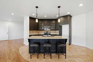 Kitchen featuring glass insert cabinets, light stone countertops, a breakfast bar, a center island with sink, and stainless steel appliances