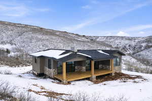 Snow covered house with stone siding, a standing seam roof, a chimney, and a deck with mountain view