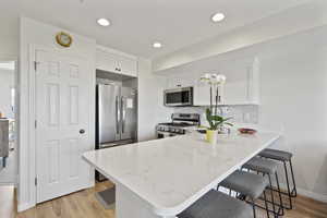 Kitchen featuring a breakfast bar area, a peninsula, light wood-style flooring, stainless steel appliances, and light stone counters
