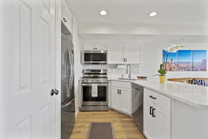 Kitchen with stainless steel appliances, white cabinets, a peninsula, and light wood finished floors