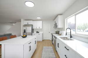 Kitchen with stainless steel appliances, a kitchen island, light wood-style flooring, and white cabinets