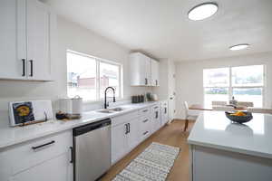 Kitchen with dishwasher, light wood-style floors, white cabinetry, and light stone counters
