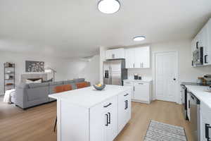 Kitchen with open floor plan, white cabinetry, light wood-style floors, a breakfast bar area, and stainless steel appliances