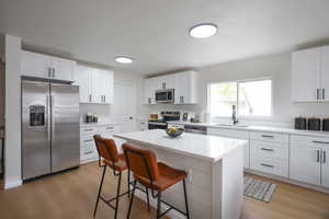 Kitchen with stainless steel appliances, a kitchen bar, white cabinetry, light wood-style floors, and a center island