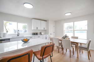Kitchen with white cabinets, light wood-style floors, stainless steel dishwasher, a breakfast bar area, and light stone countertops