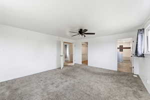 Unfurnished bedroom featuring light colored carpet, a walk in closet, and ceiling fan