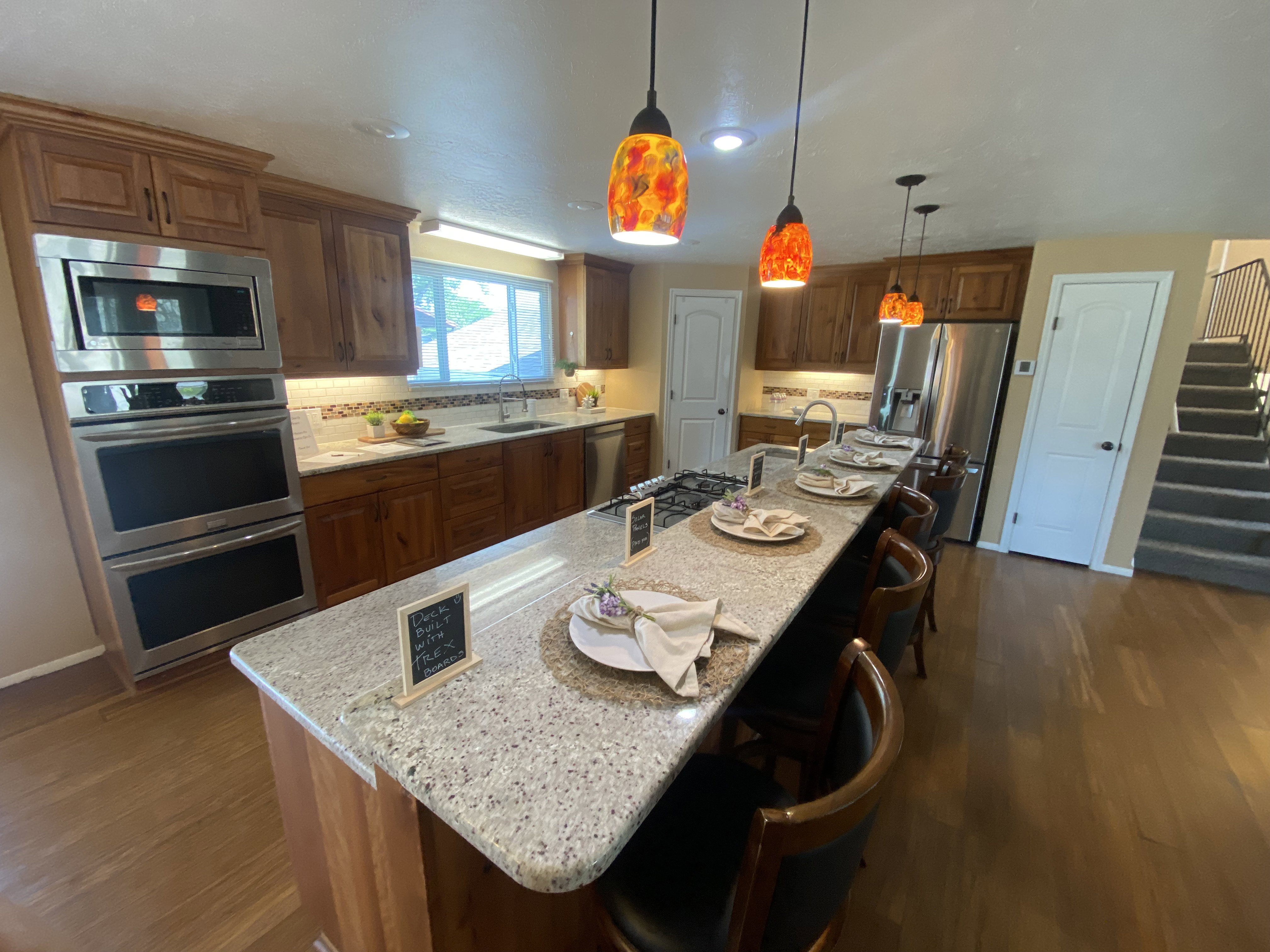 Kitchen featuring an elongated island with stone-finish countertop and seating, stainless steel appliances including double ovens and microwave, warm wood cabinetry, and wood-finish flooring