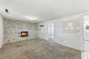 Unfurnished living room featuring a textured ceiling, carpet floors, and a stone fireplace