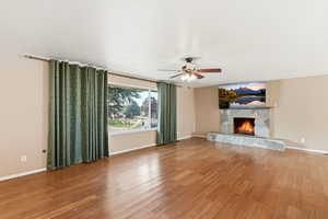 Unfurnished living room featuring ceiling fan, wood finished floors, and a fireplace