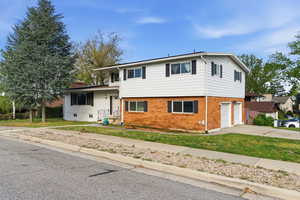 Split level home featuring brick siding, concrete driveway, a front yard, and an attached garage