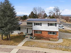 Split level home featuring roof mounted solar panels, brick siding, and a front lawn
