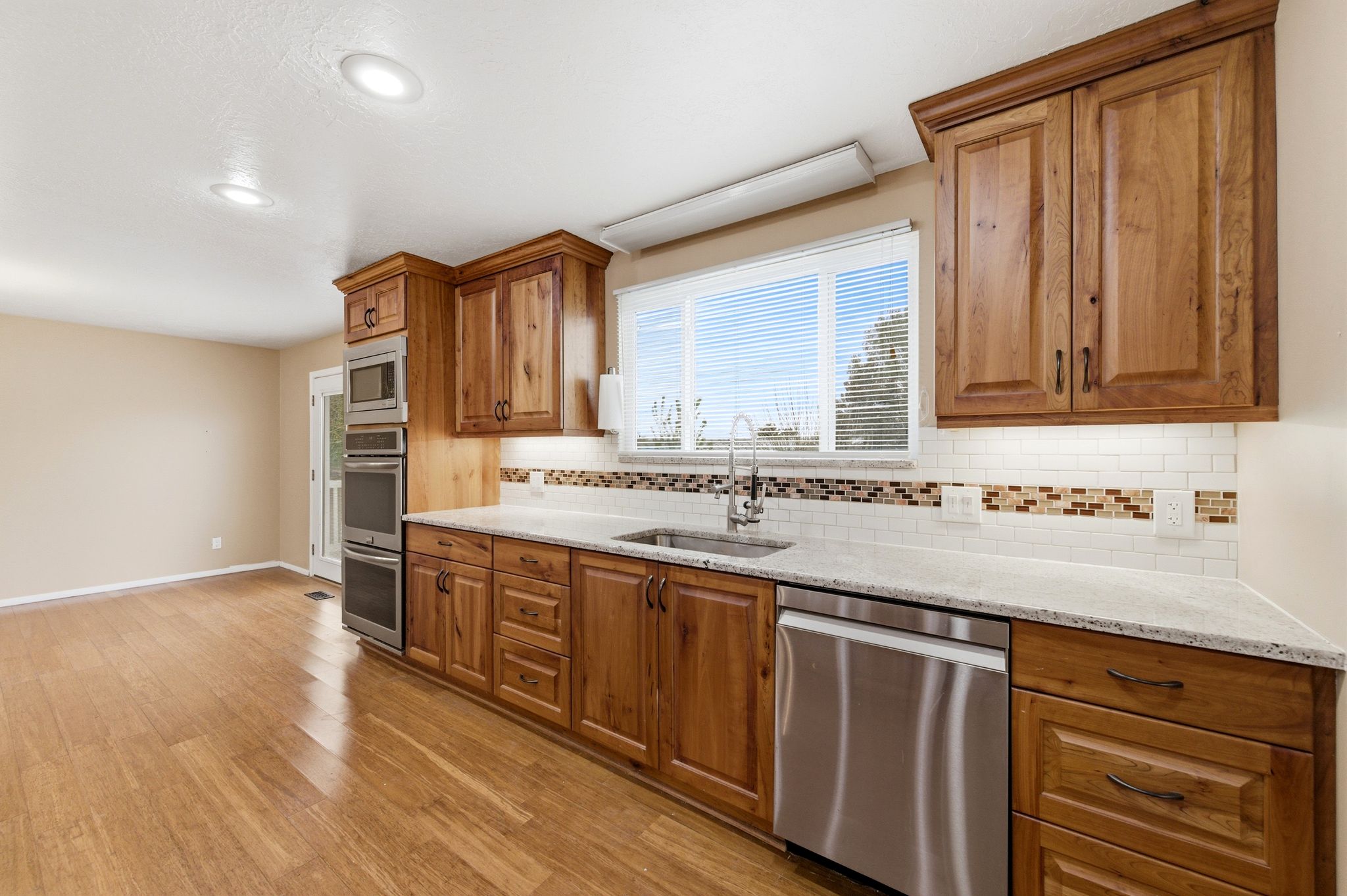 Kitchen featuring wood finish cabinets, stainless steel appliances, light stone counters, tasteful backsplash, and light wood-style floors