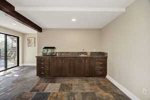 Bar featuring dark wood finish cabinetry, beamed ceiling, recessed lighting, and stone tile floors
