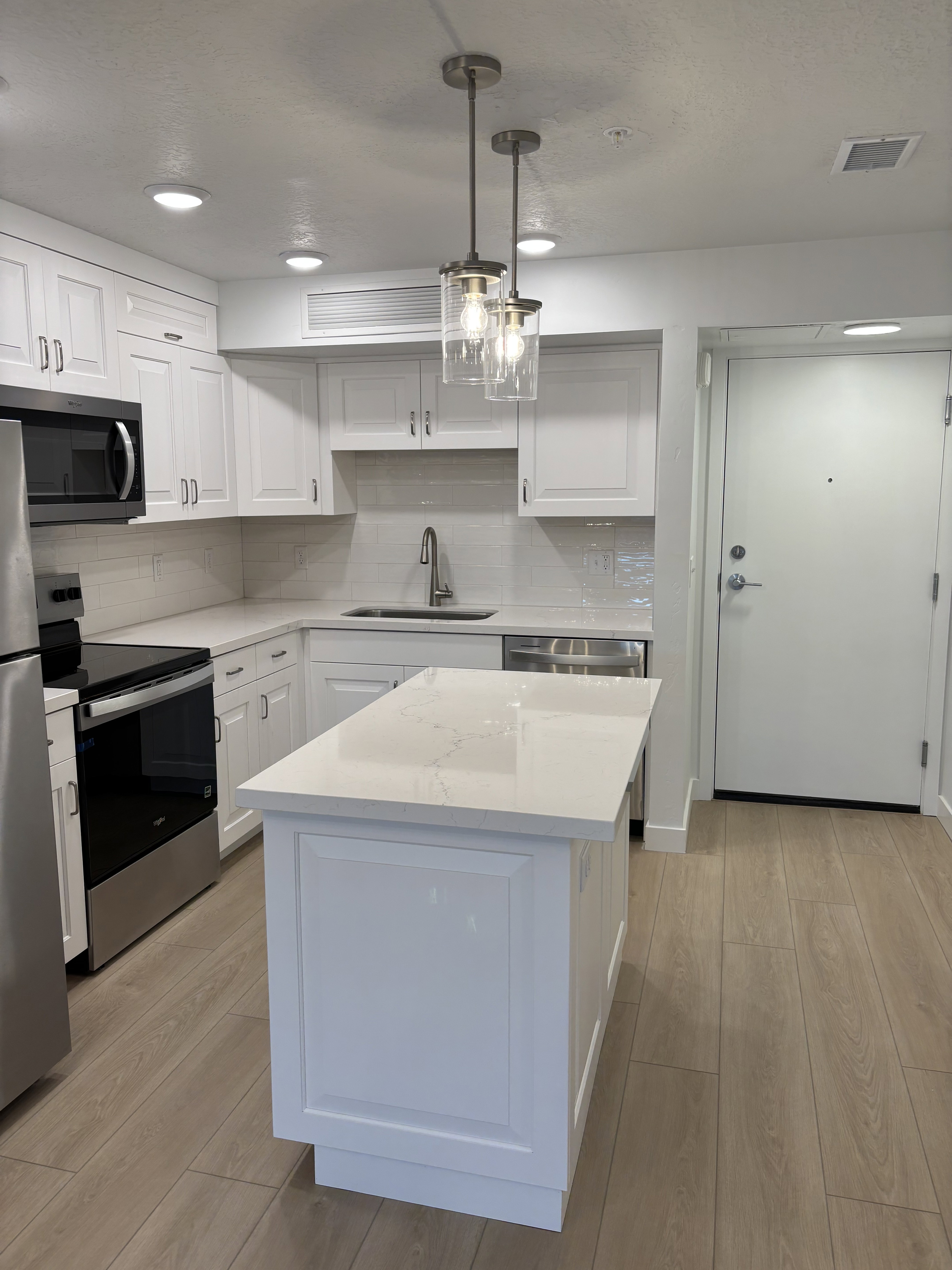 Kitchen featuring stainless steel appliances, light wood-style floors, decorative backsplash, pendant lighting, and white cabinetry