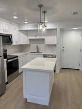Kitchen featuring stainless steel appliances, light wood-style floors, decorative backsplash, pendant lighting, and white cabinetry