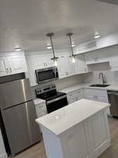Kitchen featuring stainless steel appliances, white cabinetry, a textured ceiling, pendant lighting, and decorative backsplash