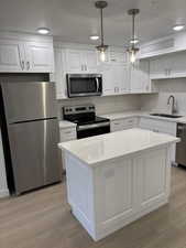 Kitchen featuring stainless steel appliances, white cabinets, hanging light fixtures, light wood-type flooring, and a center island
