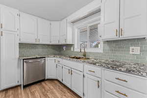 Kitchen featuring dishwasher, dark stone counters, and white cabinetry