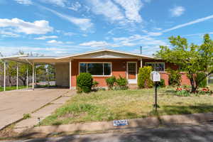 View of front of property featuring a front yard, a carport, concrete driveway, a porch, and brick siding