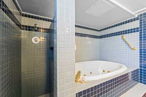 Full bath featuring a textured ceiling, tile walls, a tile shower, and a jetted tub