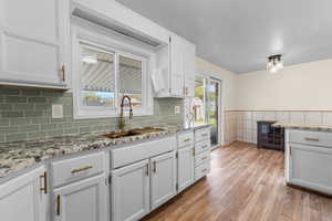 Kitchen featuring light stone counters, light wood finished floors, white cabinets, wainscoting, and tile walls