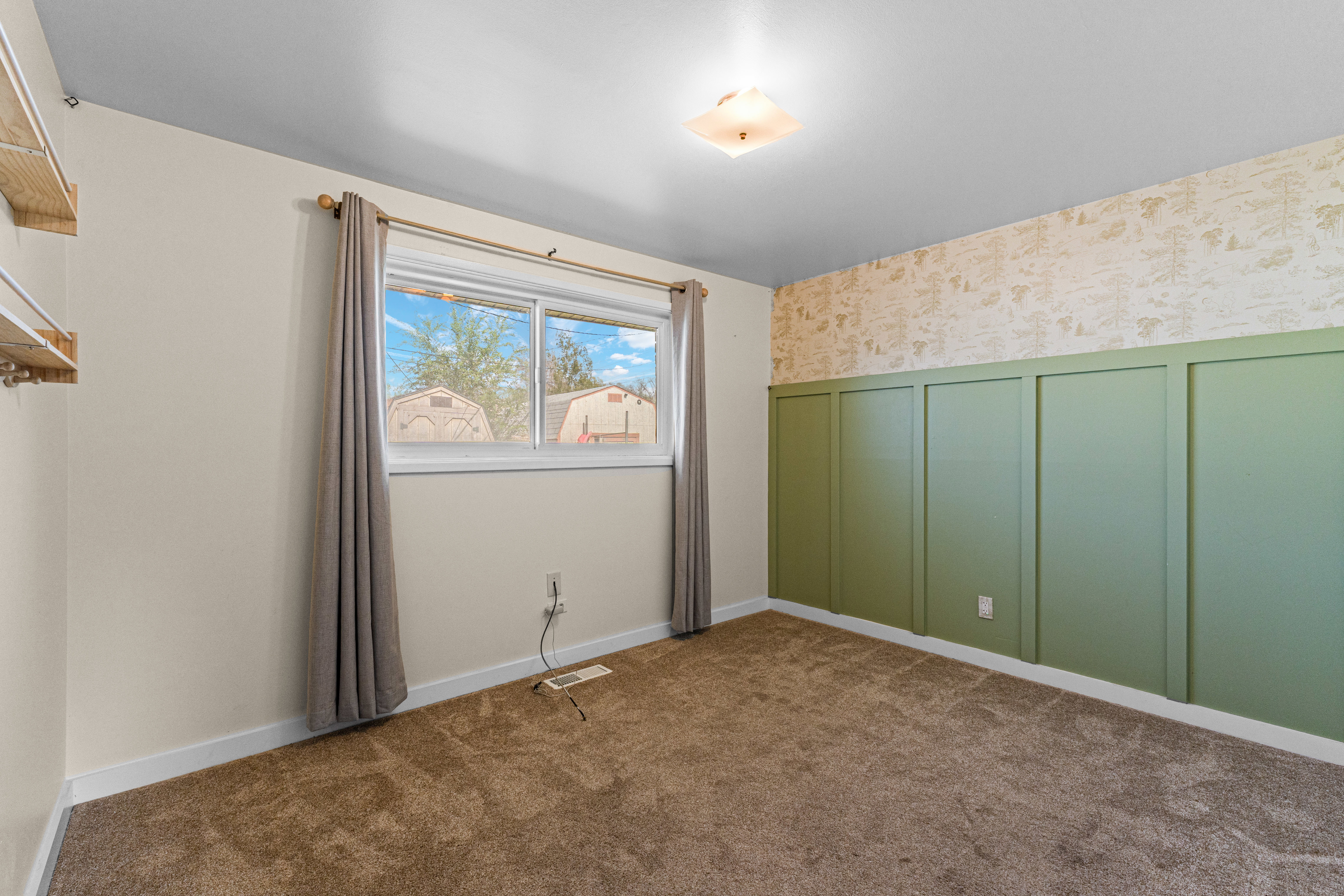 Empty room featuring wallpapered walls, a decorative wall, dark colored carpet, and wainscoting