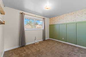 Empty room featuring wallpapered walls, a decorative wall, dark colored carpet, and wainscoting