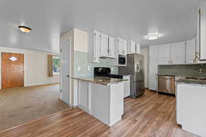 Kitchen with dark stone counters, white cabinetry, stainless steel appliances, and a peninsula