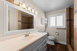 Full bath featuring vanity, dark wood-style flooring, and tiled shower