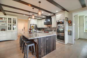 Kitchen featuring dual tone cabinets, a kitchen bar, light stone countertops, a kitchen island with sink, and light wood finished floors