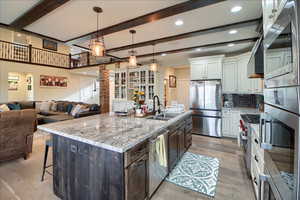 Two tone kitchen featuring dual tone cabinetry, open floor plan, stainless steel appliances, light stone countertops, and decorative backsplash