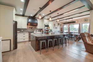 Two tone kitchen featuring dual tone cabinets, decorative light fixtures, a spacious island, light stone countertops, and a breakfast bar area