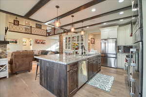 Two tone kitchen with open floor plan, dual tone cabinetry, stainless steel appliances, light stone counters, and a spacious island