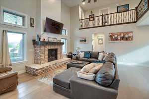 Living room featuring a high ceiling, light wood-style floors, a brick fireplace, and a ceiling fan