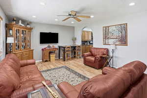 Living area featuring ceiling fan, light wood-type flooring, a textured ceiling, arched walkways, and recessed lighting
