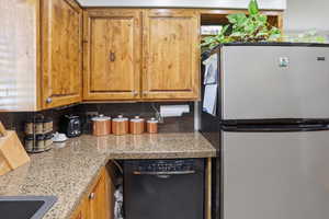 Kitchen featuring freestanding refrigerator, dishwasher, wood finish cabinets, and light stone counters