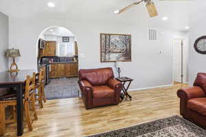 Living room with a textured ceiling, a ceiling fan, light wood-style flooring, arched walkways, and recessed lighting