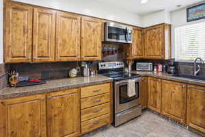 Kitchen with stainless steel appliances, wood finish cabinetry, backsplash, light tile patterned flooring, and recessed lighting