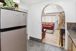 Kitchen with freestanding refrigerator, ceiling fan, arched walkways, light wood-style floors, and a textured ceiling