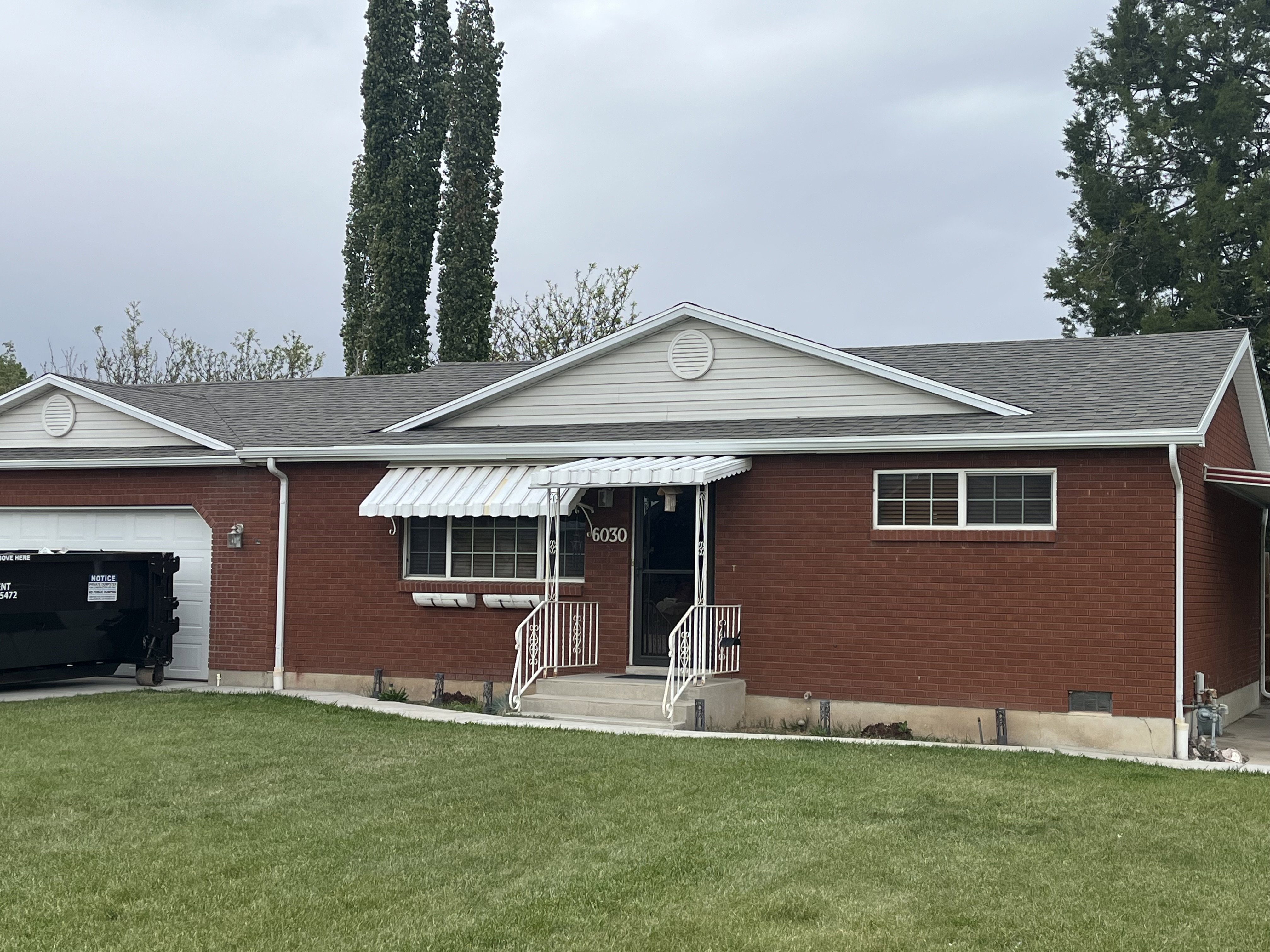 Traditional brick ranch-style residence featuring a prominent front entrance with a striped awning and white railings