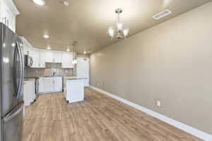 Kitchen featuring a center island, stainless steel appliances, white cabinetry, backsplash, and light stone countertops
