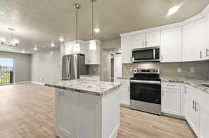 Kitchen with stainless steel appliances, white cabinetry, light wood finished floors, and a textured ceiling