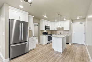 Kitchen with stainless steel appliances, a kitchen island, decorative light fixtures, white cabinets, and tasteful backsplash