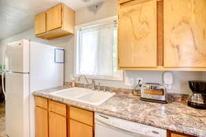 Kitchen with white appliances, light countertops, and light wood finish cabinetry